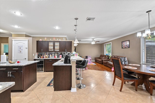 kitchen featuring decorative light fixtures, an island with sink, beverage cooler, a kitchen breakfast bar, and dark brown cabinets