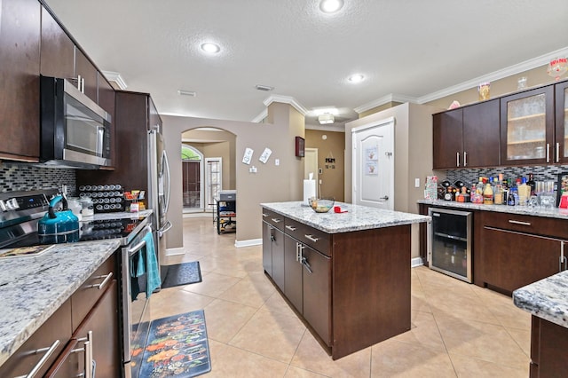 kitchen with dark brown cabinetry, light stone countertops, beverage cooler, and appliances with stainless steel finishes