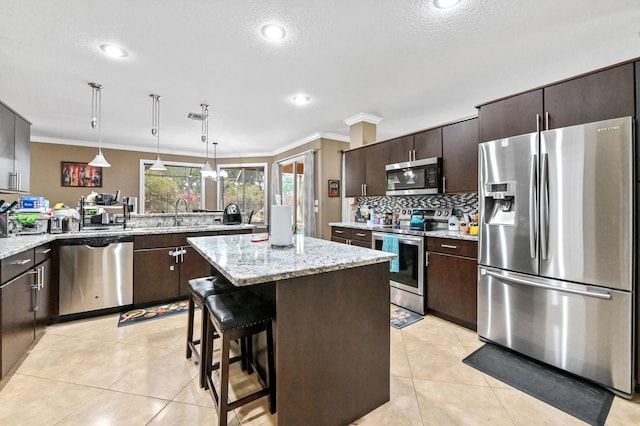 kitchen featuring light tile patterned floors, hanging light fixtures, stainless steel appliances, a center island, and dark brown cabinetry