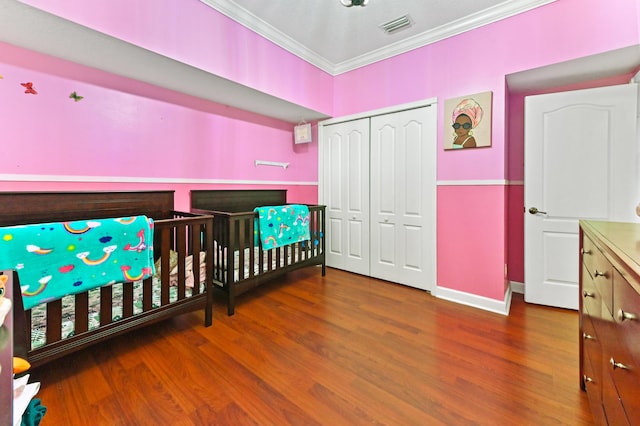 bedroom featuring crown molding, hardwood / wood-style floors, a closet, and a crib