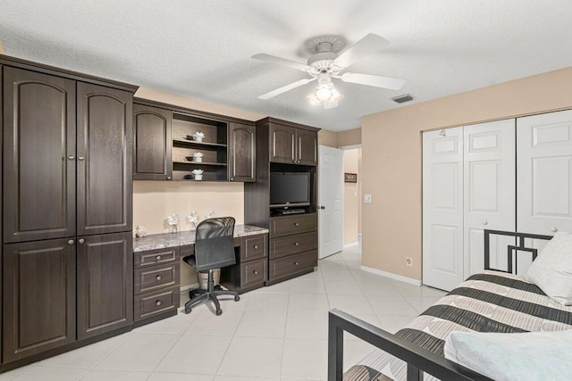 bedroom featuring light tile patterned floors, built in desk, a textured ceiling, and a closet