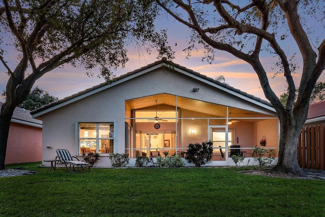 back house at dusk with ceiling fan and a yard