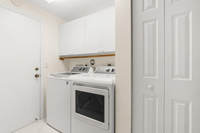 washroom with cabinets, washing machine and dryer, light tile patterned floors, and a textured ceiling