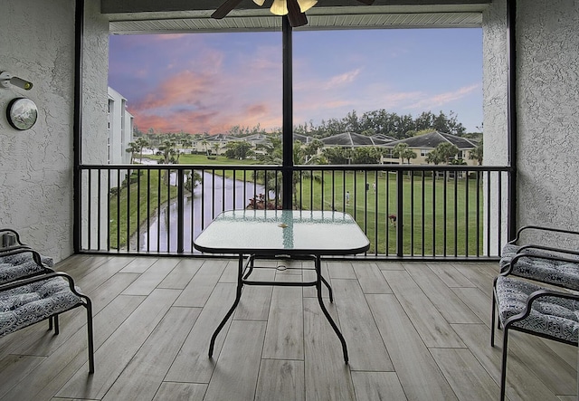 balcony at dusk featuring a water view and ceiling fan