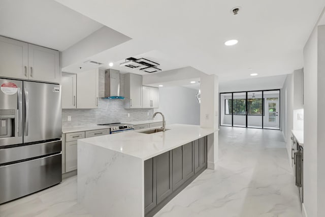 kitchen with a sink, marble finish floor, appliances with stainless steel finishes, backsplash, and wall chimney exhaust hood