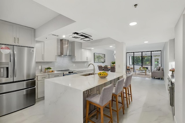 kitchen with stainless steel appliances, a sink, tasteful backsplash, marble finish floor, and wall chimney range hood