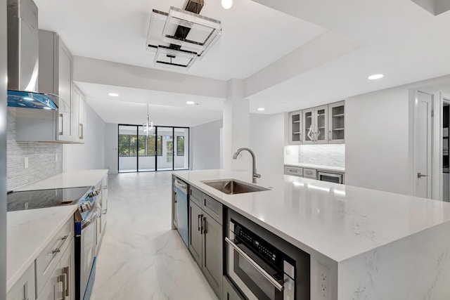 kitchen with a large island with sink, appliances with stainless steel finishes, marble finish floor, wall chimney exhaust hood, and a sink