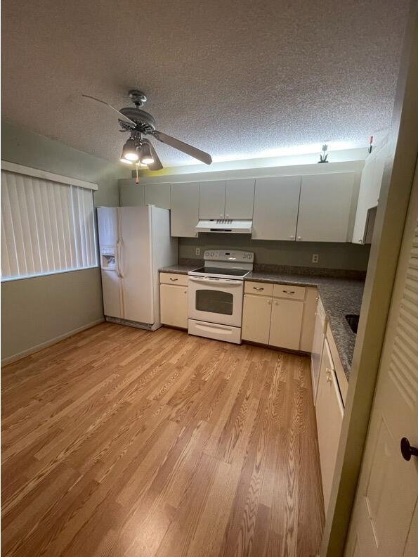 kitchen with white appliances, light hardwood / wood-style flooring, a textured ceiling, and white cabinets