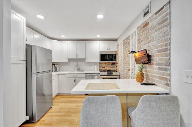 kitchen with a kitchen bar, sink, white cabinetry, kitchen peninsula, and stainless steel appliances