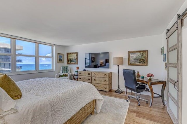 bedroom with a barn door and light wood-type flooring