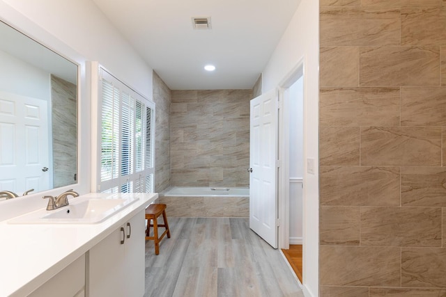 bathroom featuring a relaxing tiled tub, visible vents, wood finished floors, a tile shower, and vanity