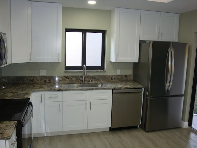 kitchen with sink, white cabinets, dark stone counters, stainless steel appliances, and light wood-type flooring