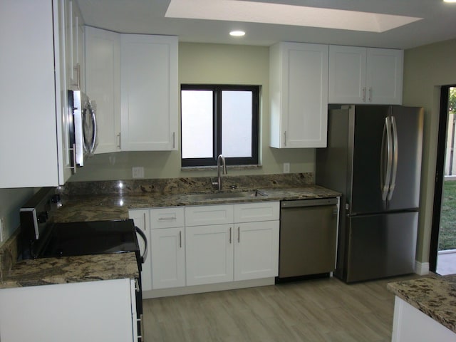 kitchen with sink, white cabinetry, stainless steel appliances, dark stone counters, and light wood-type flooring