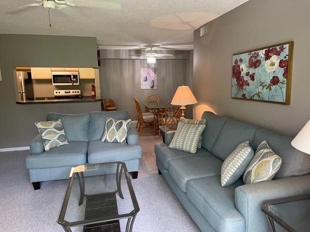 living room featuring light carpet, a textured ceiling, and ceiling fan