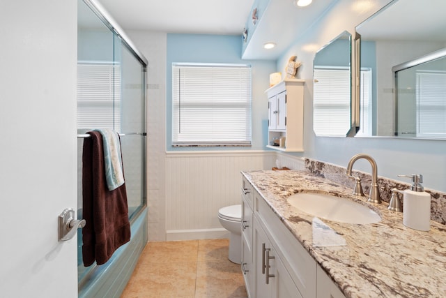 bathroom featuring wainscoting, toilet, enclosed tub / shower combo, tile patterned flooring, and vanity