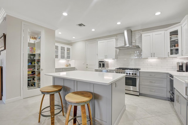 kitchen with a center island, crown molding, stainless steel range, visible vents, and wall chimney exhaust hood