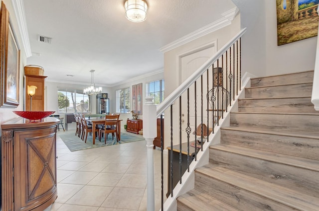 staircase featuring a textured ceiling, tile patterned flooring, a notable chandelier, visible vents, and ornamental molding