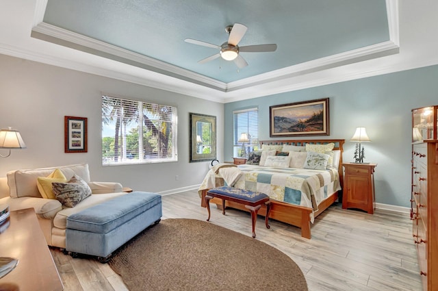 bedroom featuring ceiling fan, baseboards, ornamental molding, light wood-type flooring, and a raised ceiling