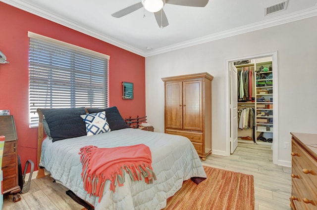 bedroom with visible vents, ornamental molding, a walk in closet, light wood-type flooring, and a closet