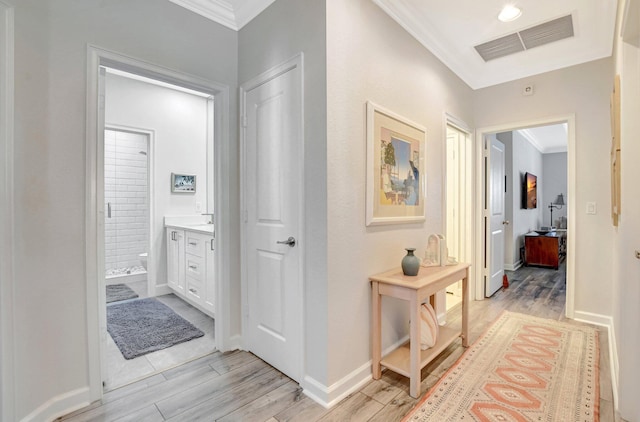 hallway featuring light wood-type flooring, visible vents, crown molding, and baseboards