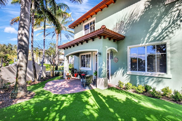 rear view of house with a tile roof, a patio, a lawn, and stucco siding