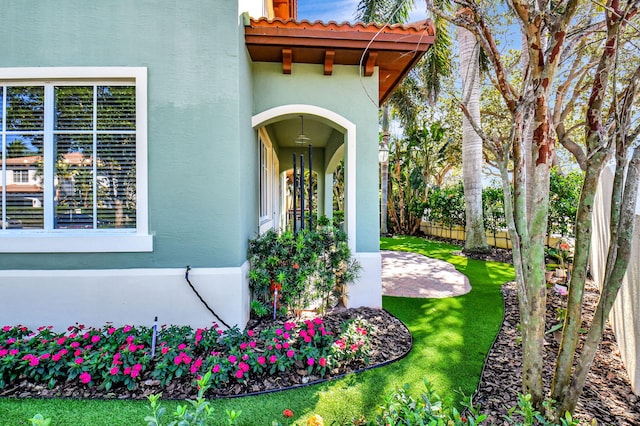 view of exterior entry with a lawn, a tiled roof, fence, a patio area, and stucco siding