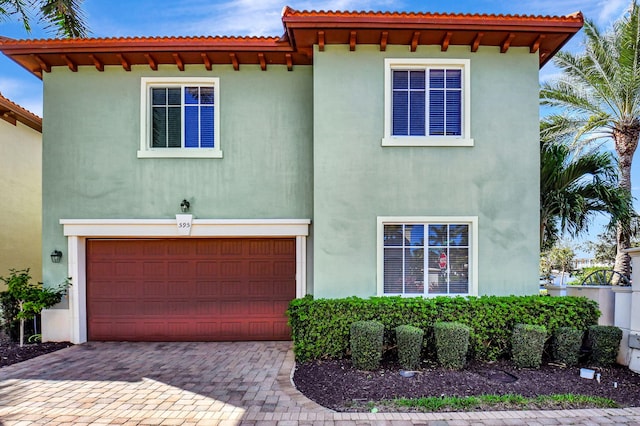 mediterranean / spanish-style home with an attached garage, decorative driveway, and stucco siding