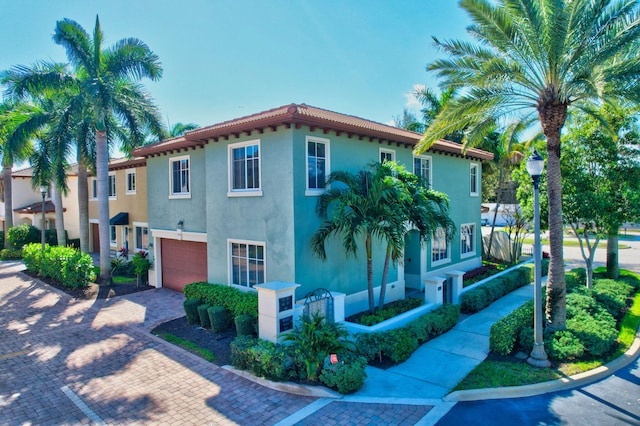 view of front of house featuring decorative driveway, a tile roof, stucco siding, fence, and a garage