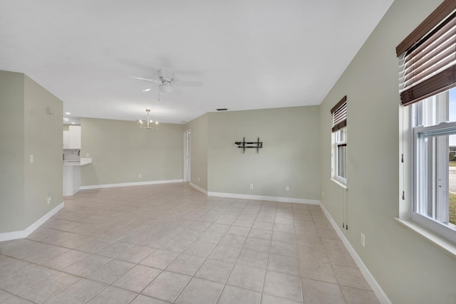 empty room with light tile patterned flooring, baseboards, ceiling fan with notable chandelier, and plenty of natural light