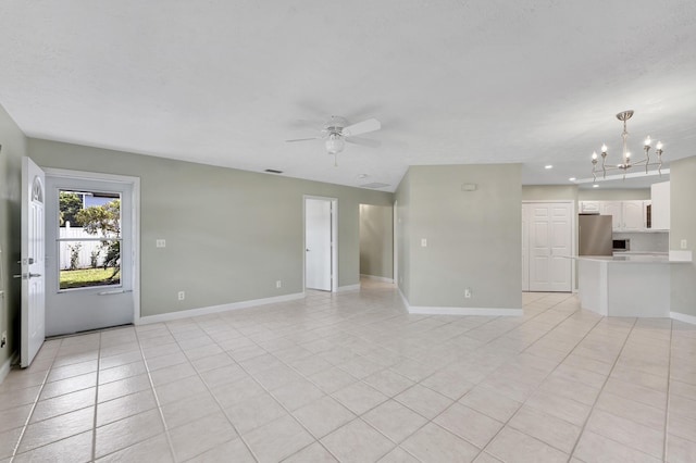 unfurnished living room with light tile patterned floors, ceiling fan with notable chandelier, and baseboards
