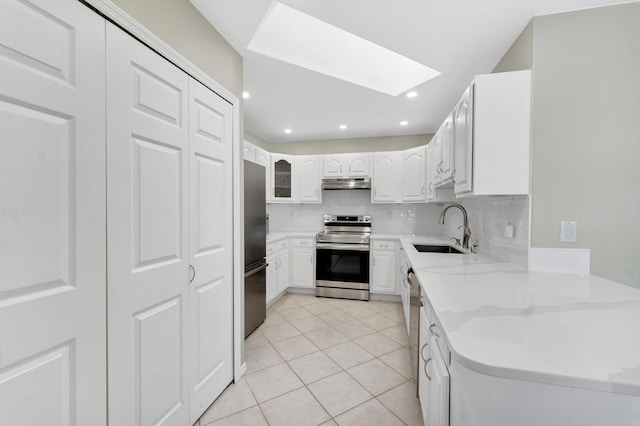 kitchen with a skylight, appliances with stainless steel finishes, under cabinet range hood, a sink, and backsplash