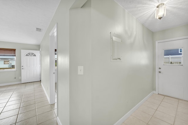 corridor with a textured ceiling, baseboards, and light tile patterned floors