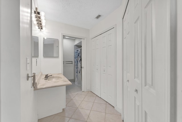bathroom featuring vanity, a textured ceiling, tile patterned floors, visible vents, and a closet