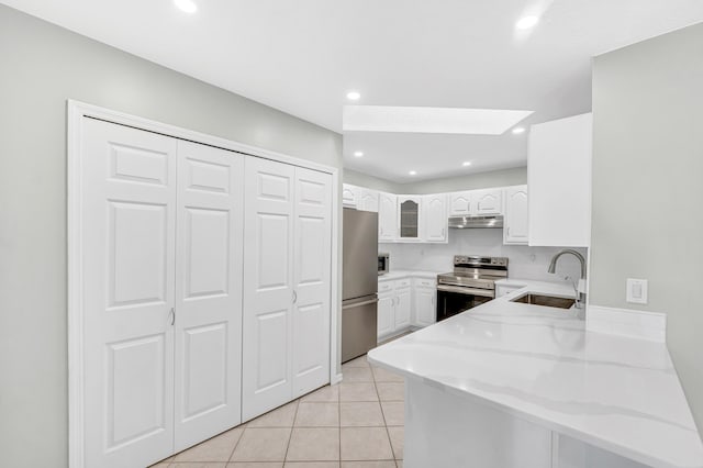 kitchen featuring a skylight, a peninsula, appliances with stainless steel finishes, a sink, and light stone counters