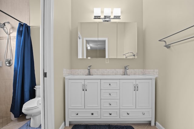 bathroom with double vanity, toilet, tiled shower, and a sink