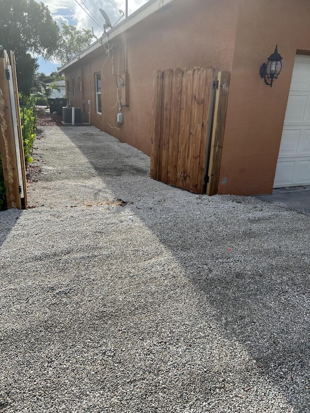 view of side of home with central air condition unit, gravel driveway, and a garage