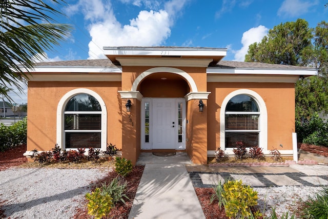 view of exterior entry featuring a shingled roof and stucco siding