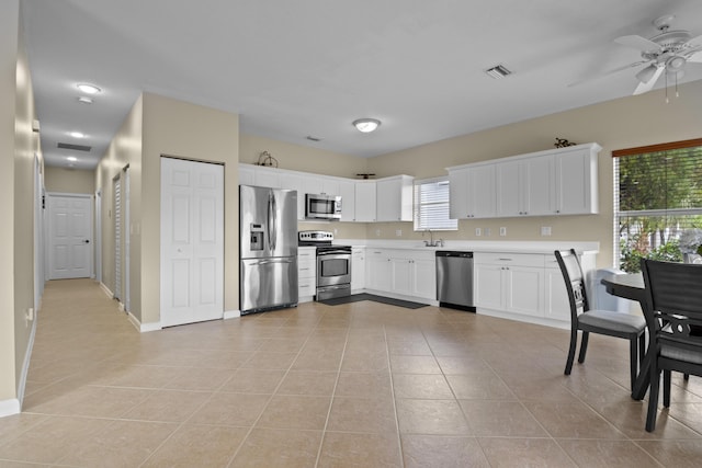 kitchen with light tile patterned floors, ceiling fan, light countertops, appliances with stainless steel finishes, and white cabinetry