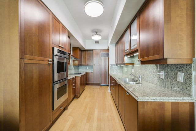 kitchen with sink, light stone counters, paneled refrigerator, double oven, and backsplash