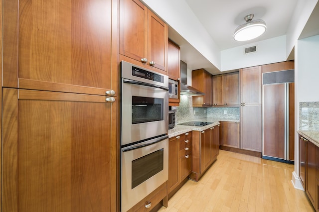 kitchen with double oven, backsplash, paneled refrigerator, light stone countertops, and wall chimney exhaust hood