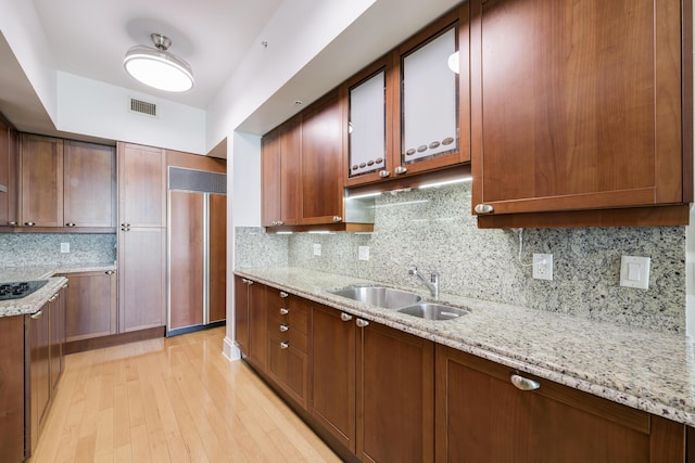 kitchen featuring paneled refrigerator, decorative backsplash, sink, and light stone counters