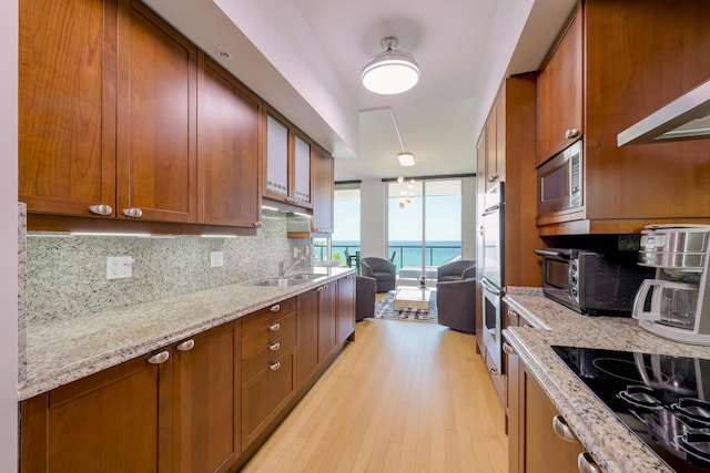 kitchen with sink, appliances with stainless steel finishes, backsplash, a water view, and light stone countertops