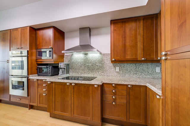 kitchen with stainless steel appliances, light stone countertops, light hardwood / wood-style floors, decorative backsplash, and wall chimney exhaust hood