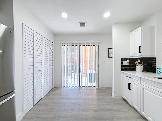 kitchen featuring stainless steel refrigerator, backsplash, white cabinets, light hardwood / wood-style floors, and a textured ceiling