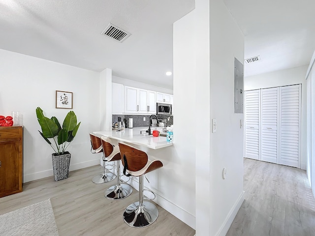 kitchen with a breakfast bar, white cabinetry, backsplash, stainless steel appliances, and kitchen peninsula