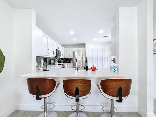 kitchen with a kitchen bar, white cabinetry, tasteful backsplash, appliances with stainless steel finishes, and kitchen peninsula