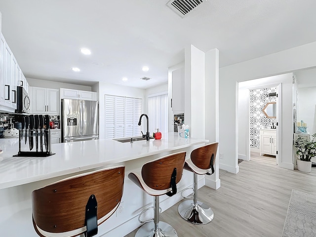 kitchen with appliances with stainless steel finishes, a breakfast bar, white cabinetry, sink, and kitchen peninsula