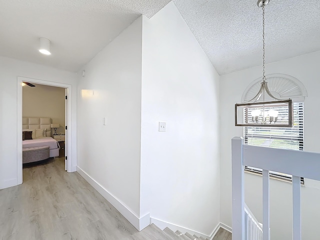 hall with lofted ceiling, light hardwood / wood-style flooring, a textured ceiling, and an inviting chandelier