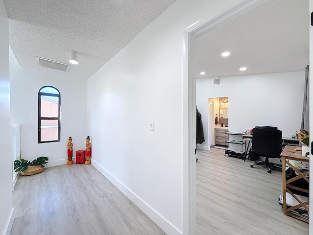 corridor featuring a textured ceiling and light hardwood / wood-style flooring