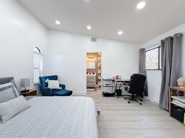 bedroom with connected bathroom, vaulted ceiling, light hardwood / wood-style flooring, and a textured ceiling